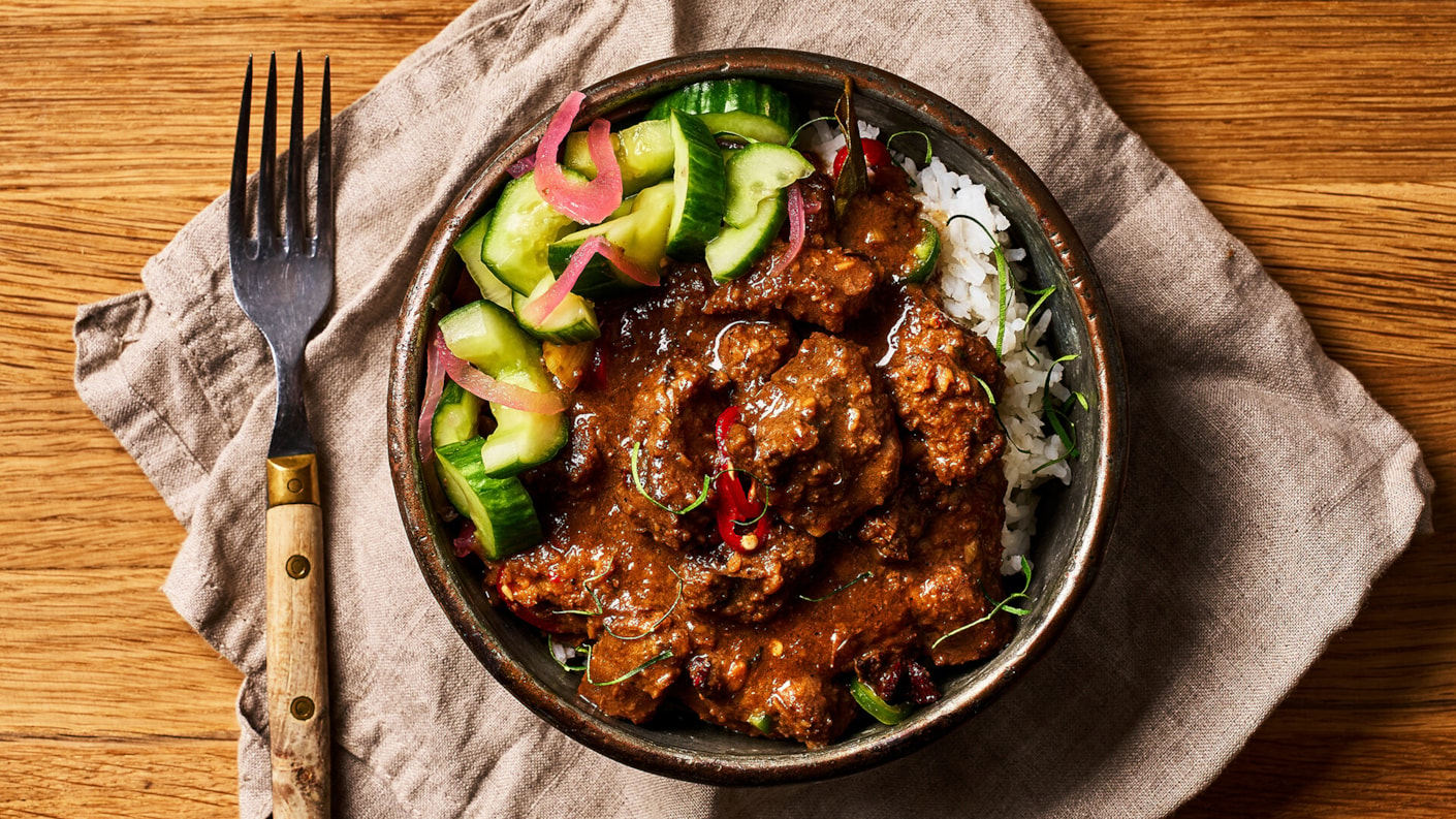 Rendang currya lautasella. Ohessa vihreitä kurkunpaloja ja pikkelöityä punasipulia.